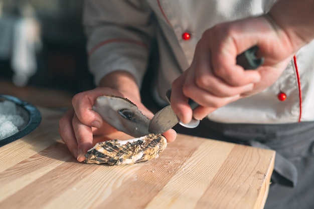 De holle en platte oesters openen. Chef-kok opent oesters in het restaurant.