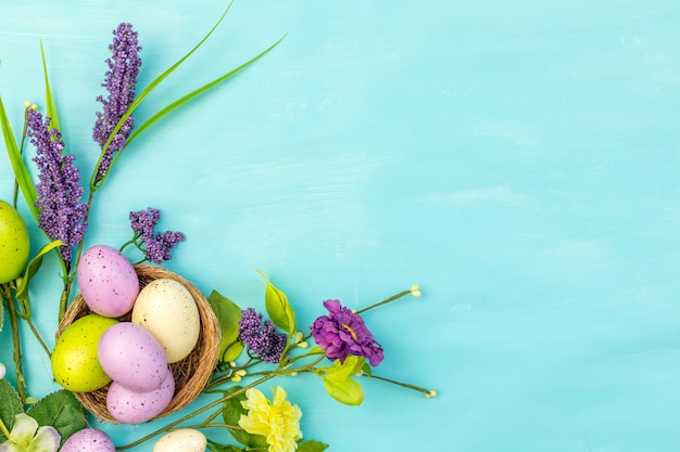 De hoogste mening van kleurrijke paaseieren in nest en springt bloemen op een turkooise achtergrond met berichtruimte op