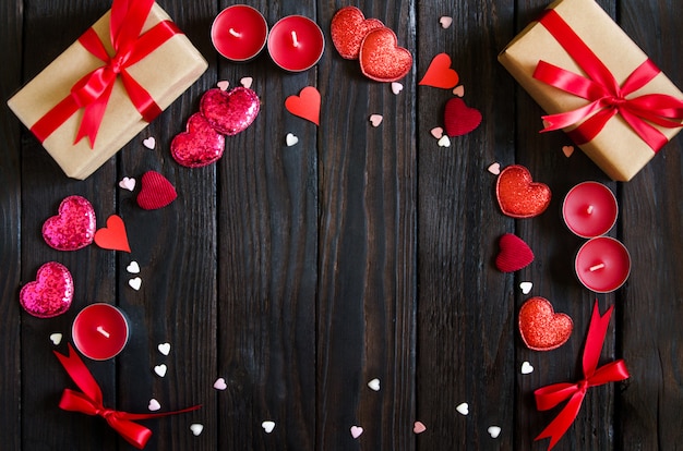 De houten achtergrond van de valentijnskaartendag met rood hart, giften en kaarsen. Cadeaus voor Valentijnsdag. Zwarte houten achtergrond