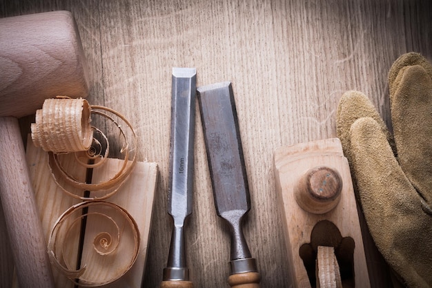 De houten bakstenenhamer krulde omhoog spaanders planer stevigere handschoenen van het beitelsleer op houten achtergrondbouwconcept