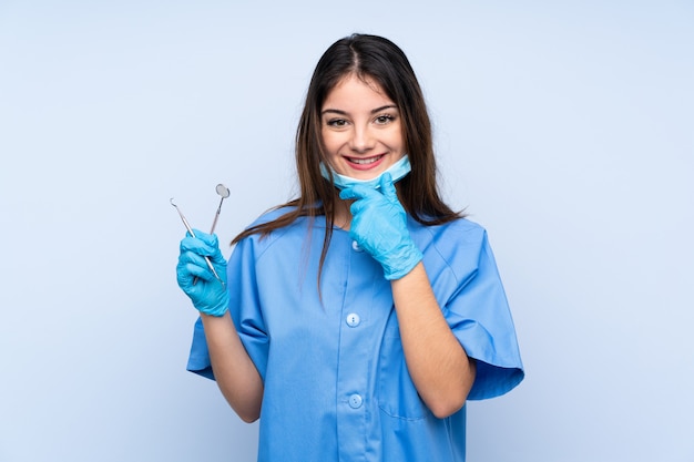 De hulpmiddelen van de de tandartsholding van de vrouw over het geïsoleerde blauwe muur lachen