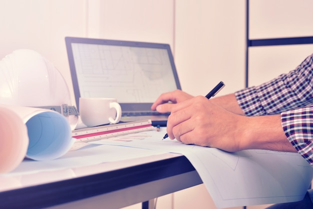 De ingenieur werkt aan het bureau met tekeningsplan