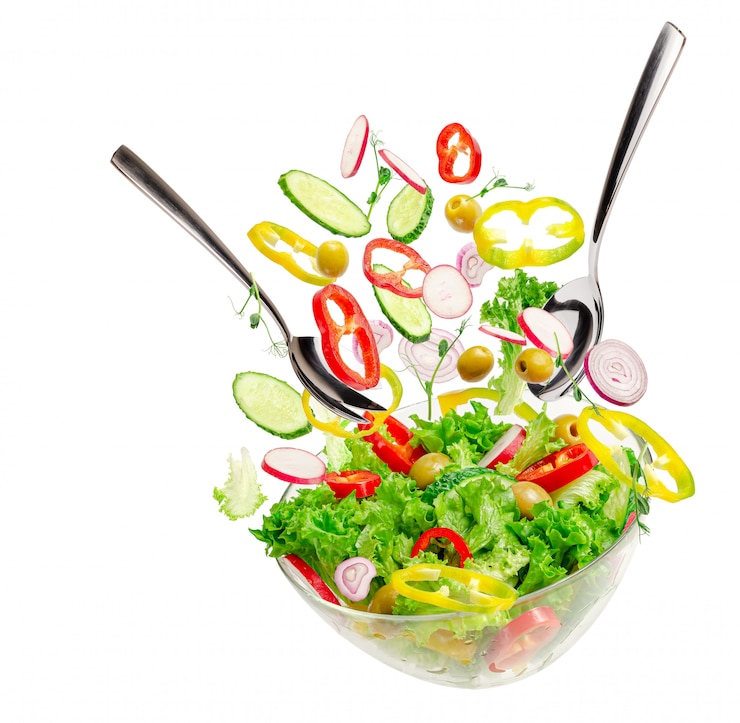 Foto de ingrediënten van de groentesalade over transparante kom met lepels vliegen. gezond uitgebalanceerd voedselconcept.
