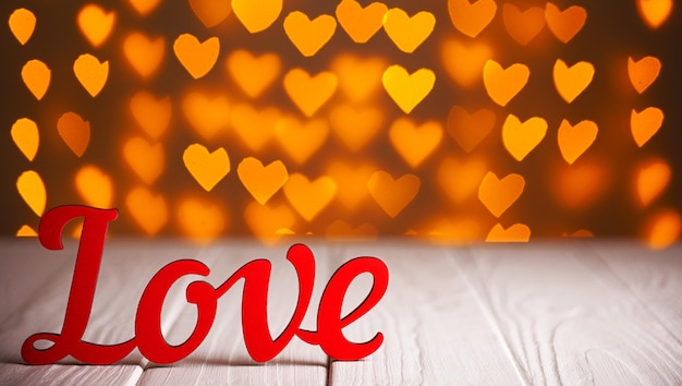 De inscriptie Love op een houten achtergrond met prachtige harten gemaakt van lampjes op een onscherpe achtergrond
