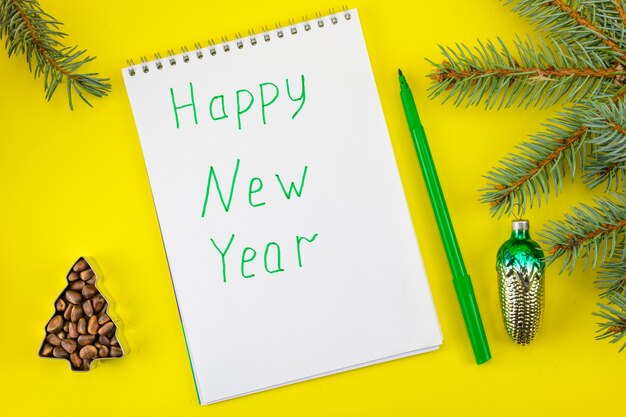 De inscriptie van het Happy New Year op de achtergrond van vuren takken, kegels en vuren noten.