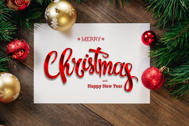 De inscriptie van Merry Christmas, groene vuren takken, decoraties, A4-blad op een houten bruine tafel. Kerstkaart, vakantie. Gemengde media.
