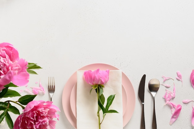 De instelling van de lentetafel met roze pioenroos bloemen op een witte tafel. Uitzicht van boven.