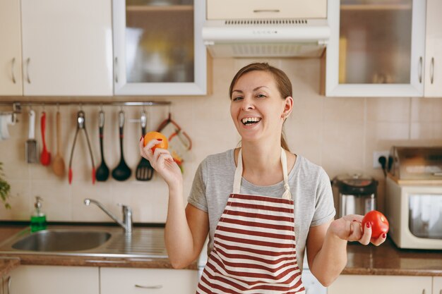 De jonge aantrekkelijke vrouw in een schort besluit een rode of gele tomaat in de keuken te kiezen. Dieet concept. Gezonde levensstijl. Thuis koken. Eten koken.