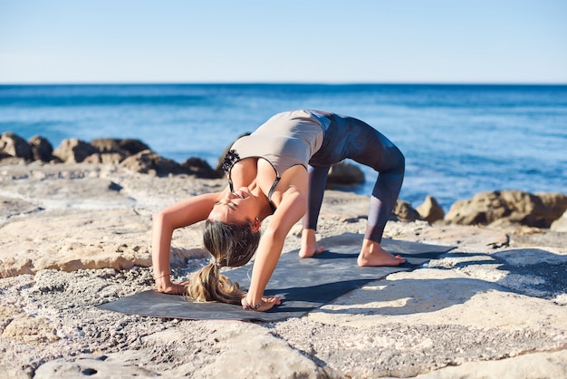 De jonge aantrekkelijke yoga van vrouwenpraktijken in wiel stelt op het strand.