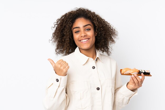 De jonge Afrikaanse Amerikaanse die sushi van de vrouwenholding op wit wordt geïsoleerd richtend aan de kant om een product voor te stellen