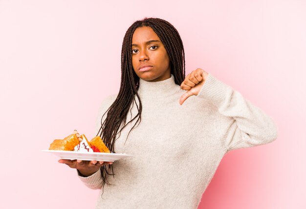 De jonge Afrikaanse Amerikaanse vrouw die een wafel geïsoleerd houden het tonen van een afkeergebaar, duimen neer. Meningsverschil concept.
