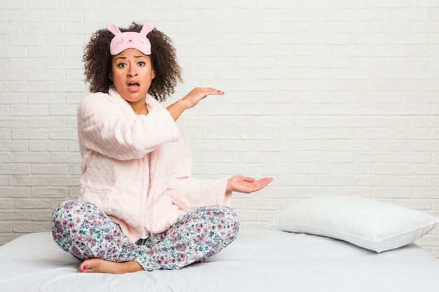 De jonge Afrikaanse Amerikaanse vrouw in bed droeg pijama en verbaasde het houden van tussen handen.