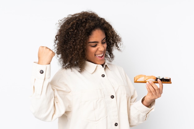 De jonge Afro-Amerikaanse sushi van de vrouwenholding op witte muur die een overwinning vieren