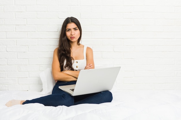 De jonge Arabische vrouw die met haar laptop aan het bed fronsende gezicht in ongenoegen werken, houdt wapens gevouwen.