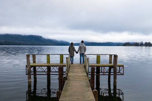 De jonge Aziatische handen van de paarholding op het brugmeer Te Anau New Zealand