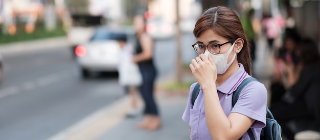 De jonge Aziatische vrouw die ademhalingsmasker N95 draagt beschermt en filtert pm2.5 (deeltjes) tegen verkeer en stofstad. gezondheidszorg en luchtvervuiling concept