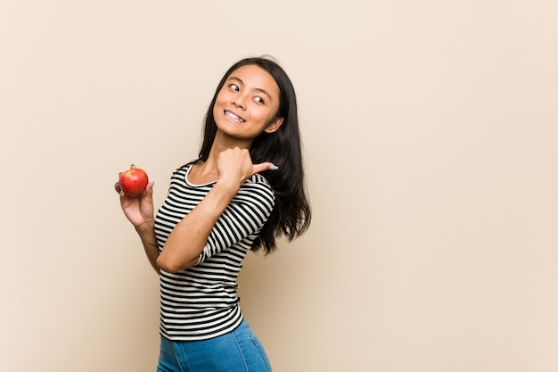 De jonge Aziatische vrouw die een appel houden richt met duimvinger weg, lachend en onbezorgd.