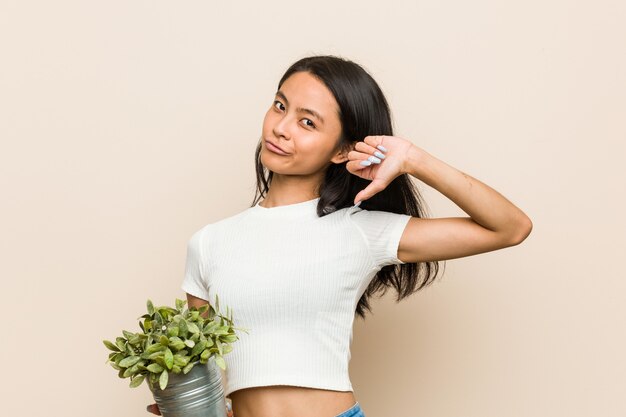 De jonge Aziatische vrouw die een plant vasthoudt, voelt zich trots en zelfverzekerd, voorbeeld om te volgen.