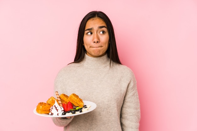 De jonge Aziatische vrouw die een wafel houdt isoleert verward, voelt twijfelachtig en onzeker.