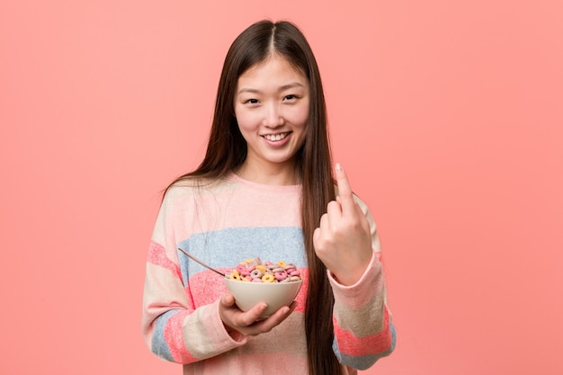 De jonge Aziatische vrouw met een graangewassenkom richt met vinger op u alsof uitnodigend dichterbij kom.