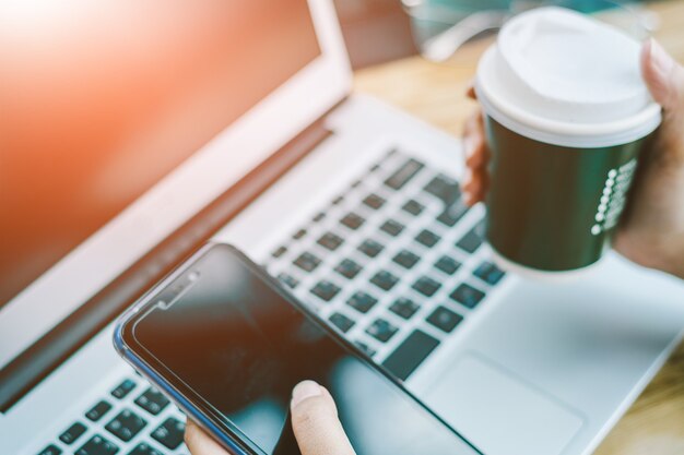 De jonge Aziatische zakenman werkt aan slimme telefoon in bureau met laptop. Online winkelen.