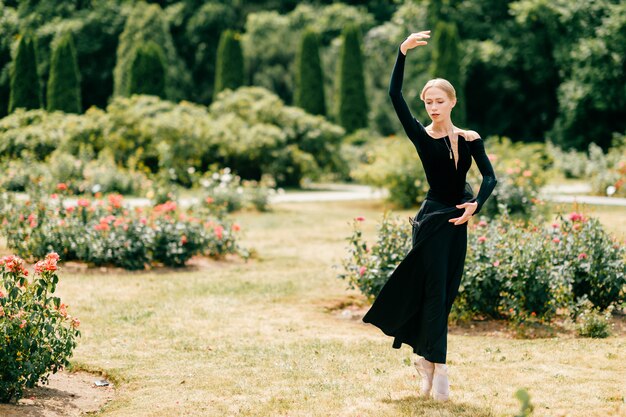 De jonge ballerina in zwarte kleding die en ballet stellen stellen stelt in de zomerpark