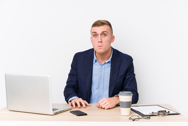 De jonge bedrijfsmens met laptop haalt schouders op en opent verwarde ogen.