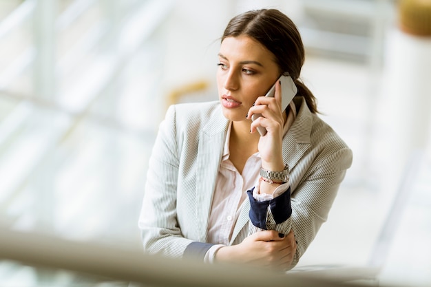 De jonge bedrijfsvrouw bevindt zich op de treden op het kantoor en gebruikt mobiele telefoon