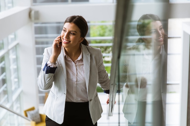 De jonge bedrijfsvrouw bevindt zich op de treden op het kantoor en gebruikt mobiele telefoon