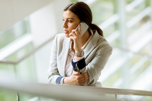 De jonge bedrijfsvrouw bevindt zich op de treden op het kantoor en gebruikt mobiele telefoon