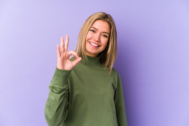 De jonge blonde Kaukasische vrouw isoleerde vrolijk en zeker tonend ok gebaar.