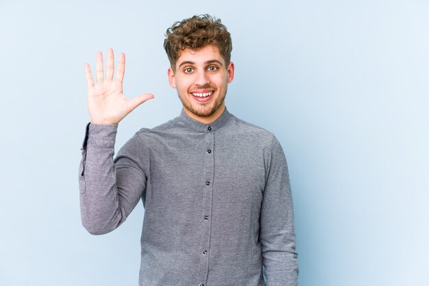 De jonge blonde krullende haar Kaukasische mens isoleerde het glimlachen vrolijk tonend nummer vijf met vingers.