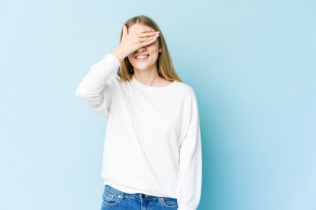 De jonge blonde vrouw behandelt ogen met handen, in grote lijnen glimlacht wachtend op een verrassing.