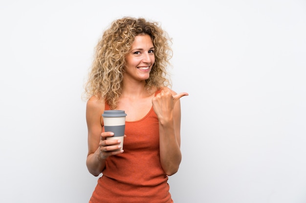 De jonge blondevrouw die met krullend haar houden haalt koffie weg richtend aan de kant om een product te presenteren