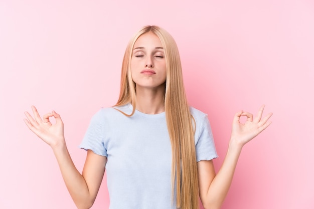 De jonge blondevrouw op roze muur ontspant na harde werkdag, voert zij yoga uit.