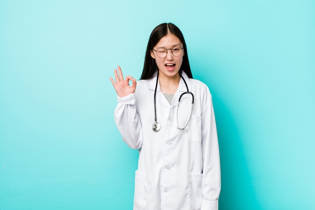 De jonge Chinese artsenvrouw knipoogt en houdt een ok gebaar met hand.