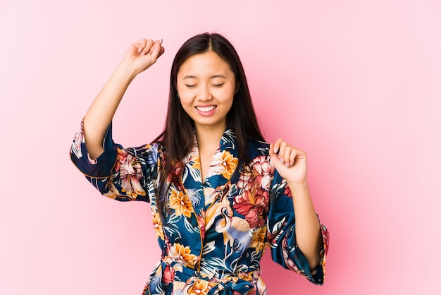 De jonge Chinese vrouw die een kimonopyjama draagt isoleerde het vieren van een speciale dag, sprongen en heft wapens met energie op.