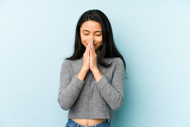 De jonge Chinese vrouw die op een blauwe muurholding wordt geïsoleerd dient binnen bidt dichtbij mond, voelt zeker.