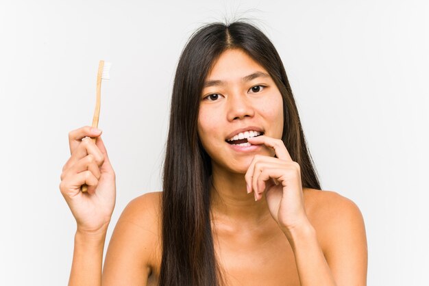 De jonge Chinese vrouw die tandenborstel geïsoleerd houden ontspande het denken over iets bekijkend een exemplaarruimte.