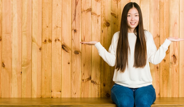 De jonge Chinese vrouwenzitting op een houten plaats maakt schaal met wapens, voelt gelukkig en zeker.