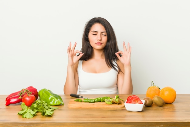 De jonge curvy vrouw die een gezonde maaltijd voorbereidt ontspant na harde werkdag, voert zij yoga uit.