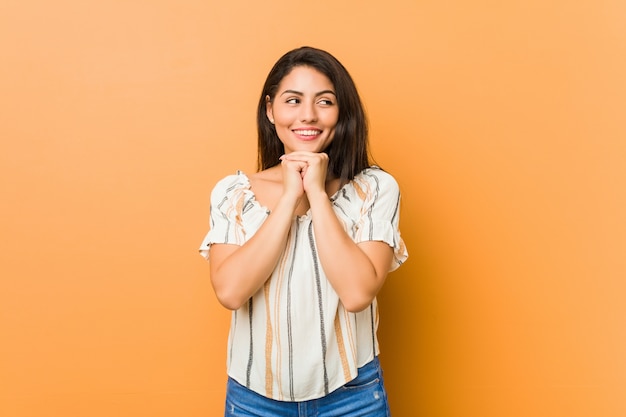 De jonge curvy vrouw houdt handen onder kin, kijkt gelukkig opzij.