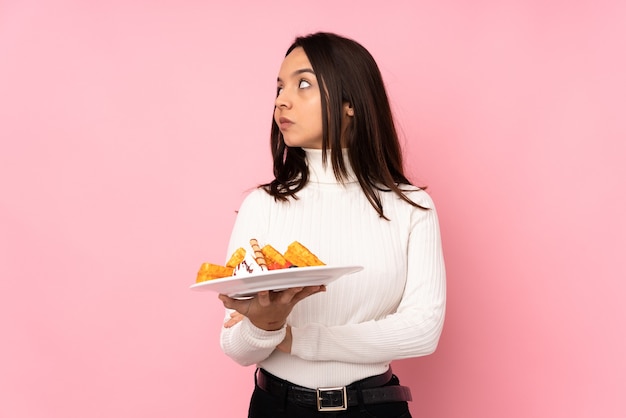 De jonge donkerbruine wafels van de vrouwenholding over geïsoleerd roze portret als achtergrond