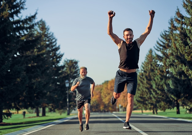 De jonge en oude sporters die op de weg rennen