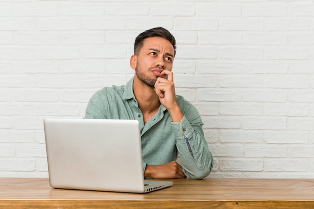 De jonge filipijnse mensenzitting die met zijn laptop werken ontspande het denken over iets bekijkend een exemplaarruimte.