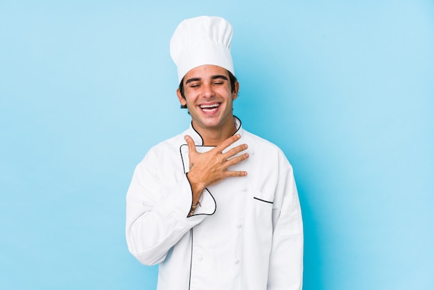 De jonge geïsoleerde kokmens lacht hardop hand houdend op borst.