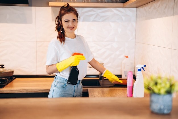 De jonge gelukkige leuke vrouw in gele handschoenen maakt thuis haar keuken schoon.