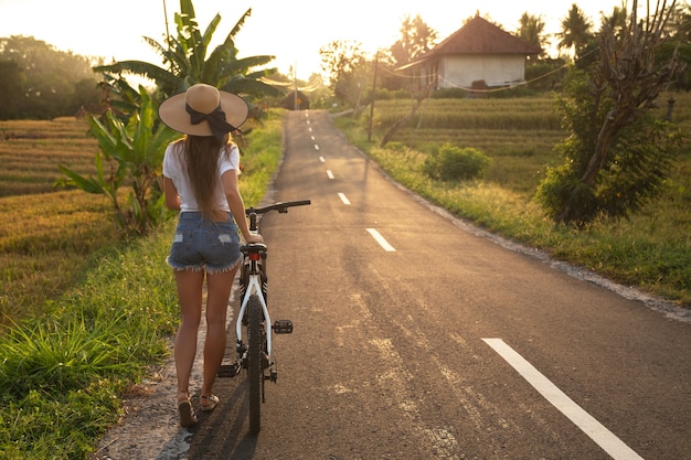 De jonge gelukkige vrouw loopt met een fiets door smalle landweg