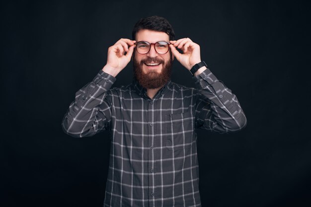 De jonge glimlachende mens die baard draagt zet op zijn oogglazen.