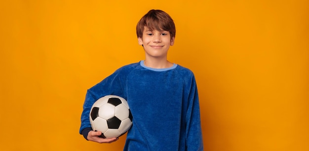 De jonge glimlachende tienerjongen houdt een voetbal of een voetbalbal met één wapen